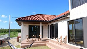 A modern house with a patio, outdoor seating, and a large window. - Ishigaki Island Villa 7716 (Ishigaki)