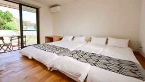 A double bed with patterned bedding, a wooden floor, a small table, and a sliding glass door leading to an outdoor area. - Ishigaki Island Villa 7716 (Ishigaki)