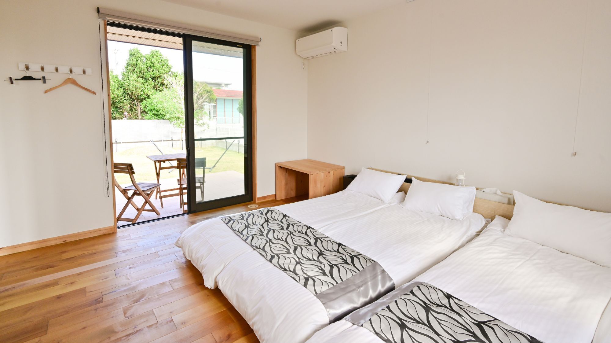 A bedroom with a large bed, a wooden desk, a chair, and a sliding glass door leading to an outdoor area.