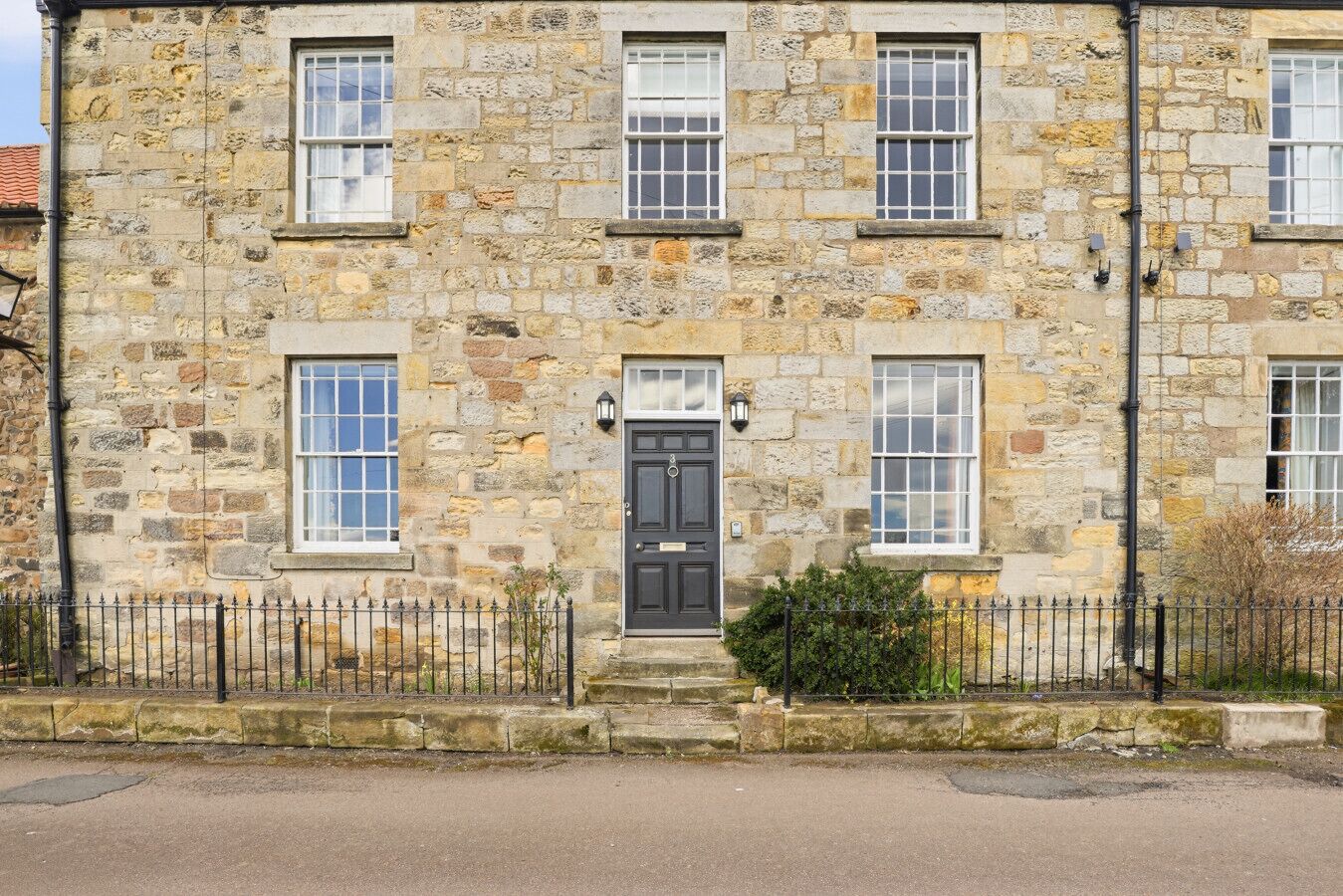 A stone building with a central door, multiple windows, and a black metal fence.