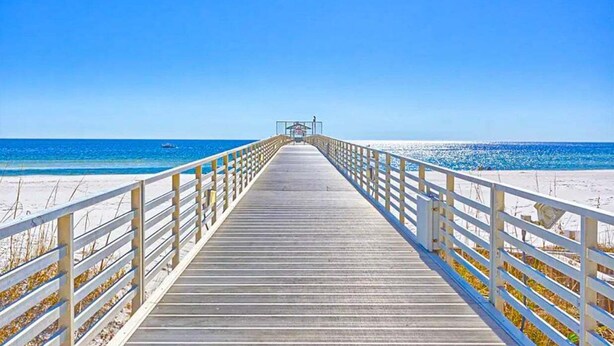 Una banchina di legno che conduce a una spiaggia sotto un cielo azzurro limpido.