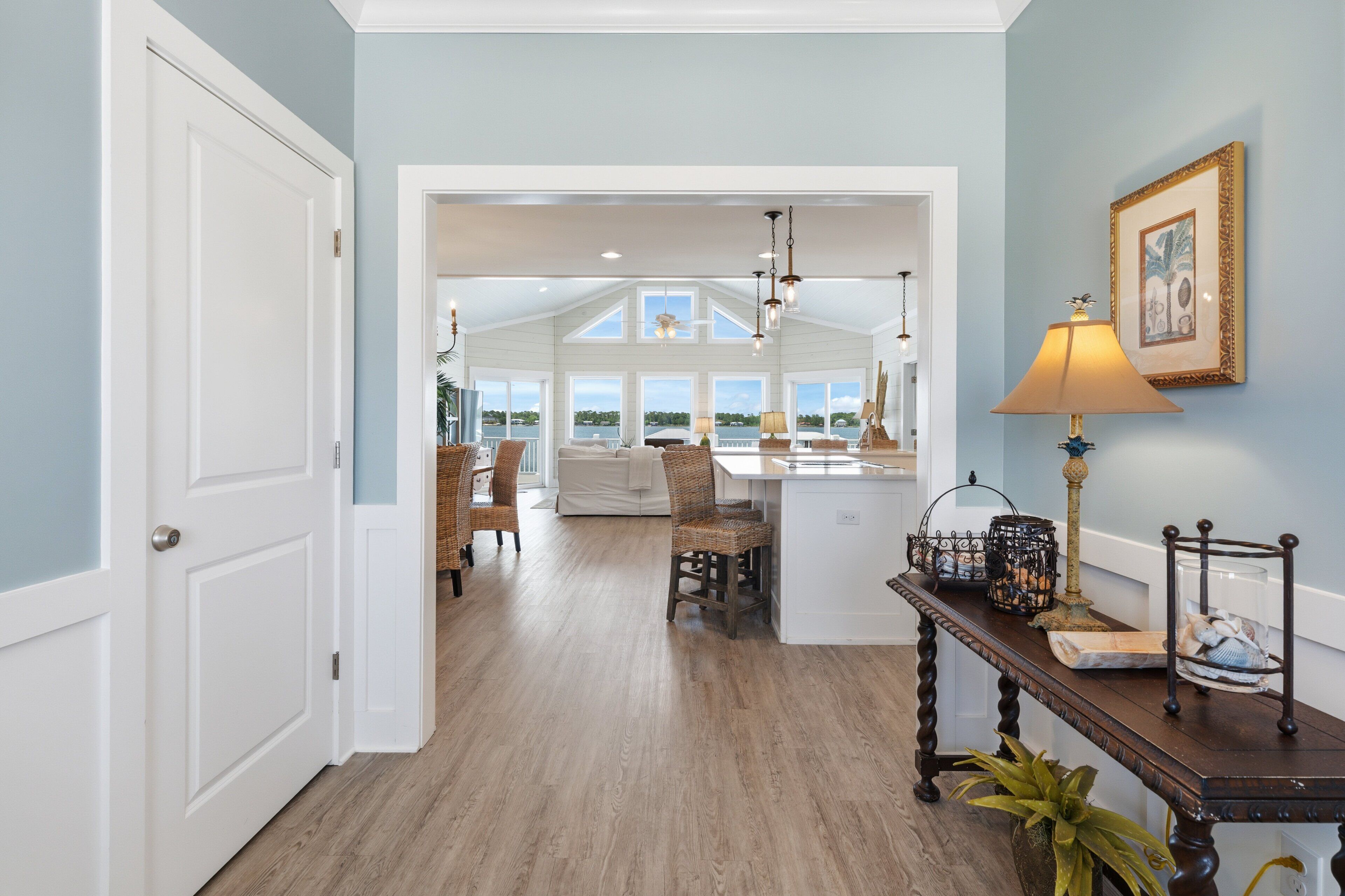A spacious hallway with a view to a dining area, a white door, and a table with decorative items.