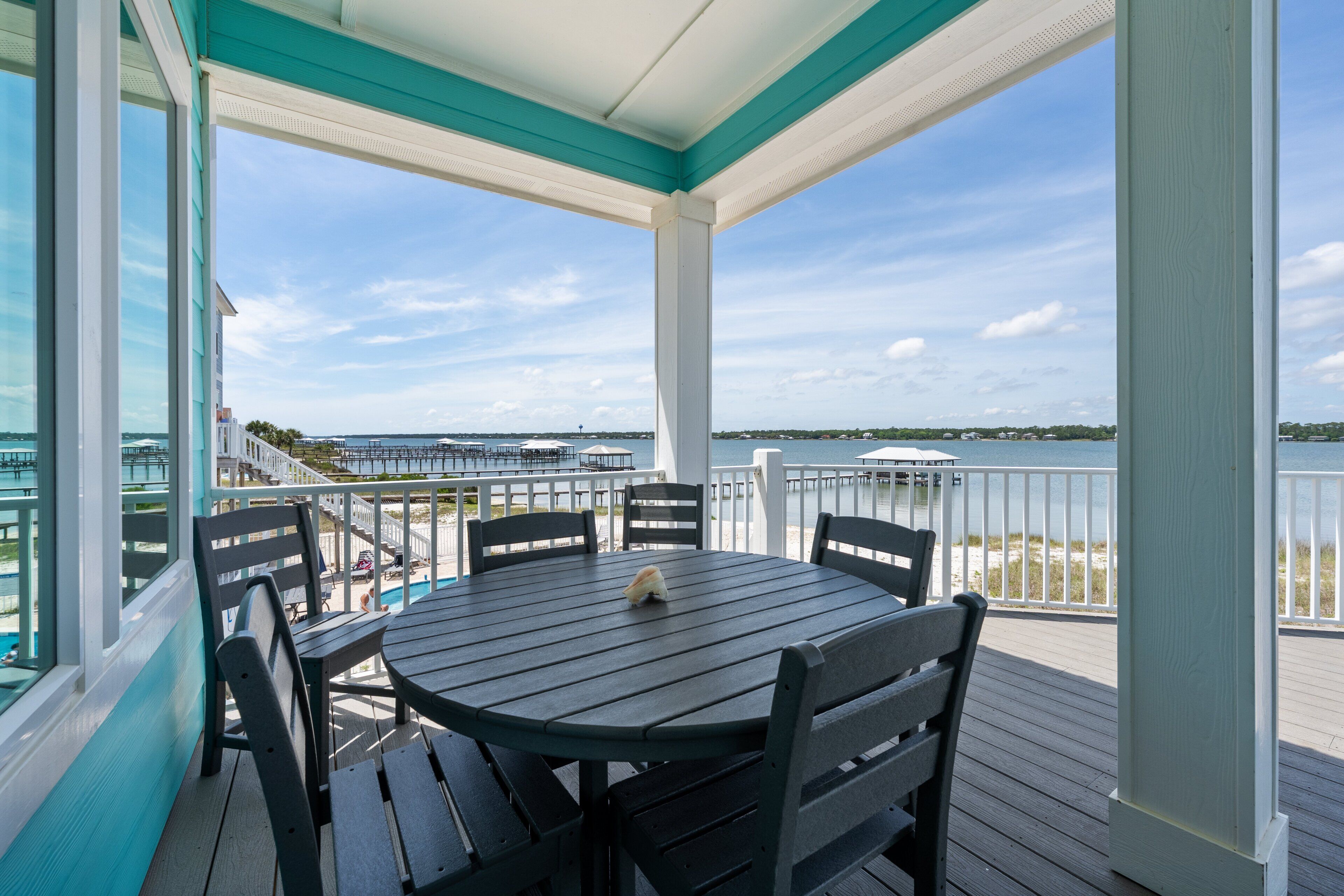 A covered outdoor area with a table and chairs, overlooking a body of water and a distant shoreline.