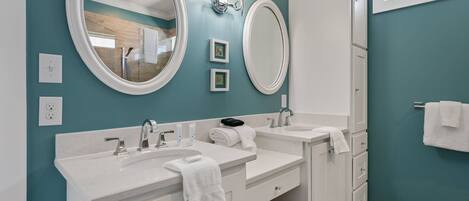 A bathroom with two sinks, a large mirror, wall sconces, and a towel rack.