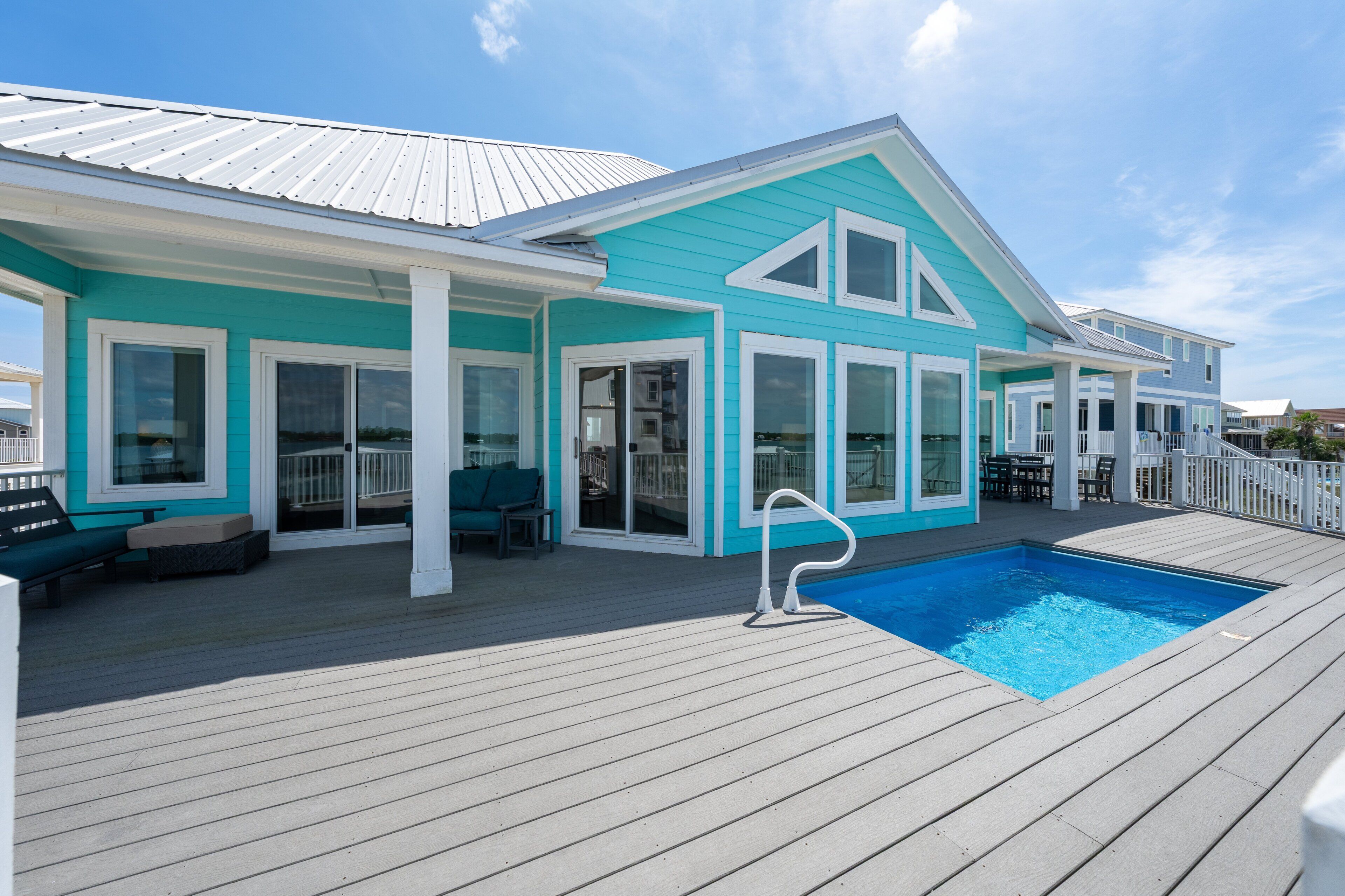 Ein türkisfarbenes Haus mit Swimmingpool auf einer Holzterrasse.