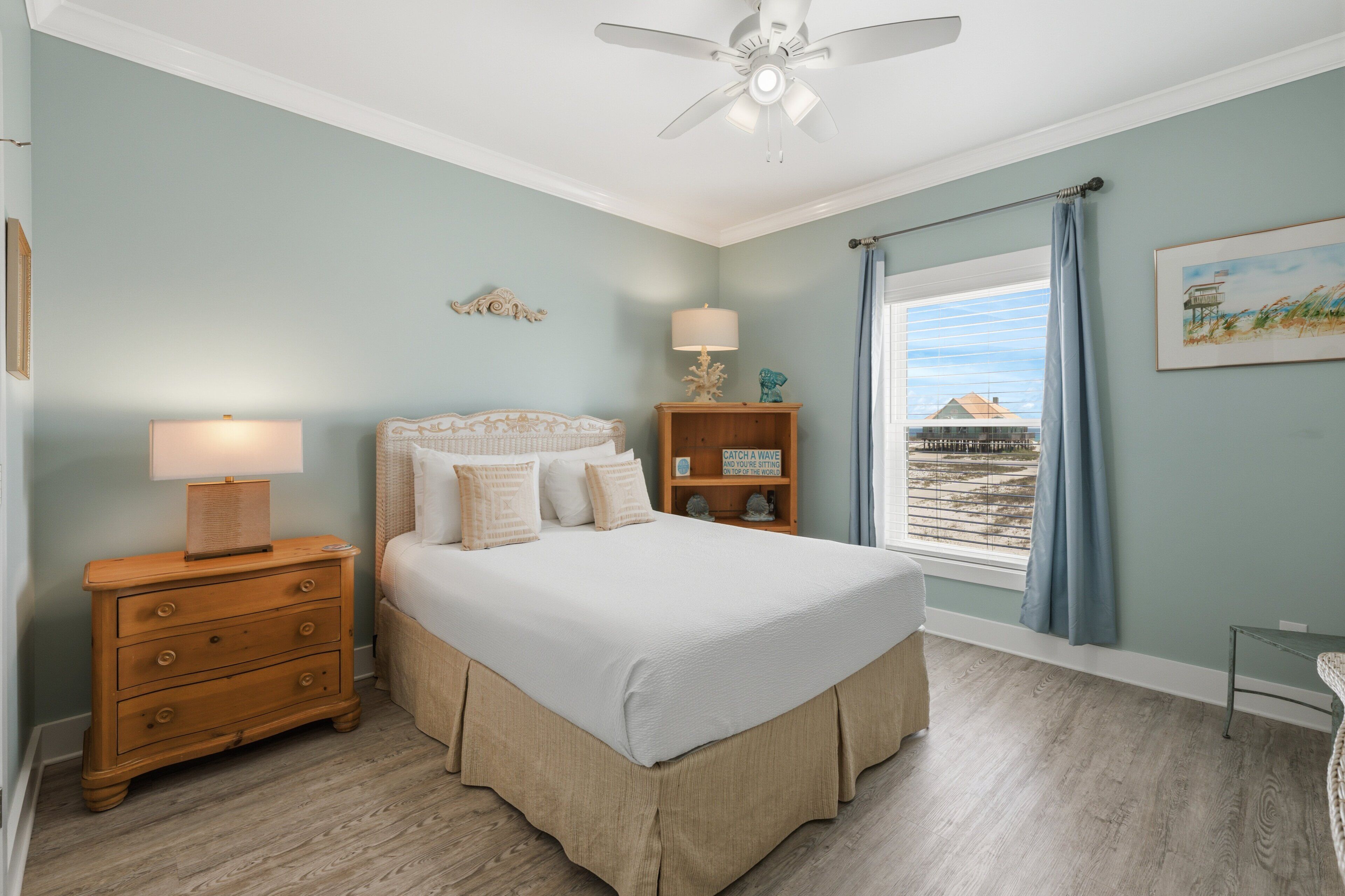 A bedroom with a bed, nightstand, lamp, and a view of the beach.