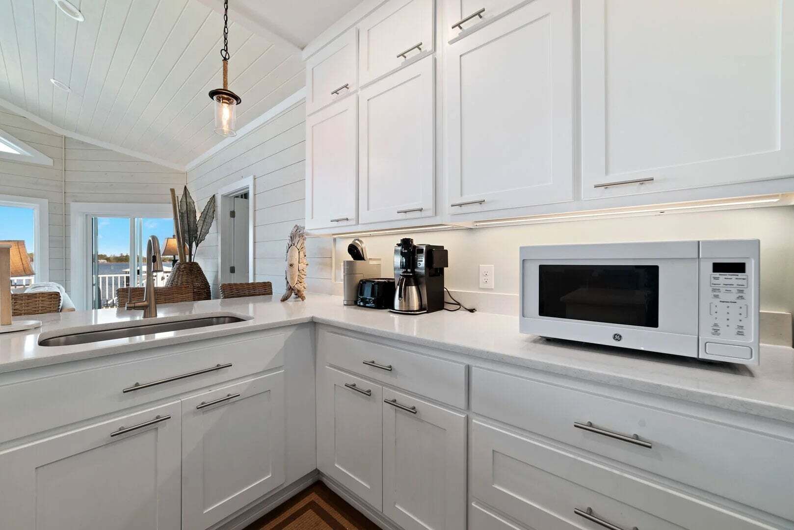 A modern kitchen with white cabinetry, a built-in microwave, and a coffee maker.