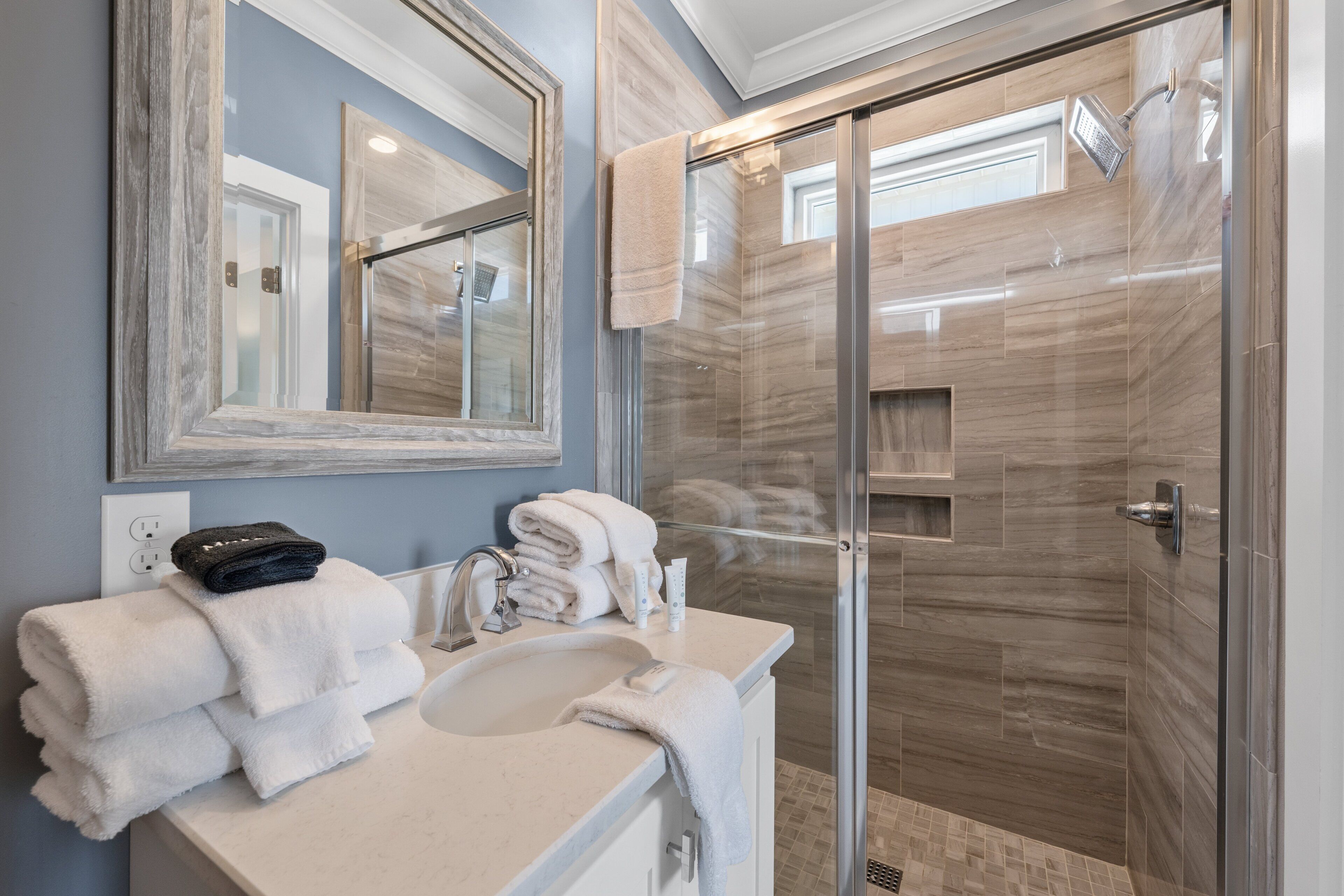 Un baño moderno con cabina de ducha de vidrio, un lavabo con espejo y una pila de toallas.