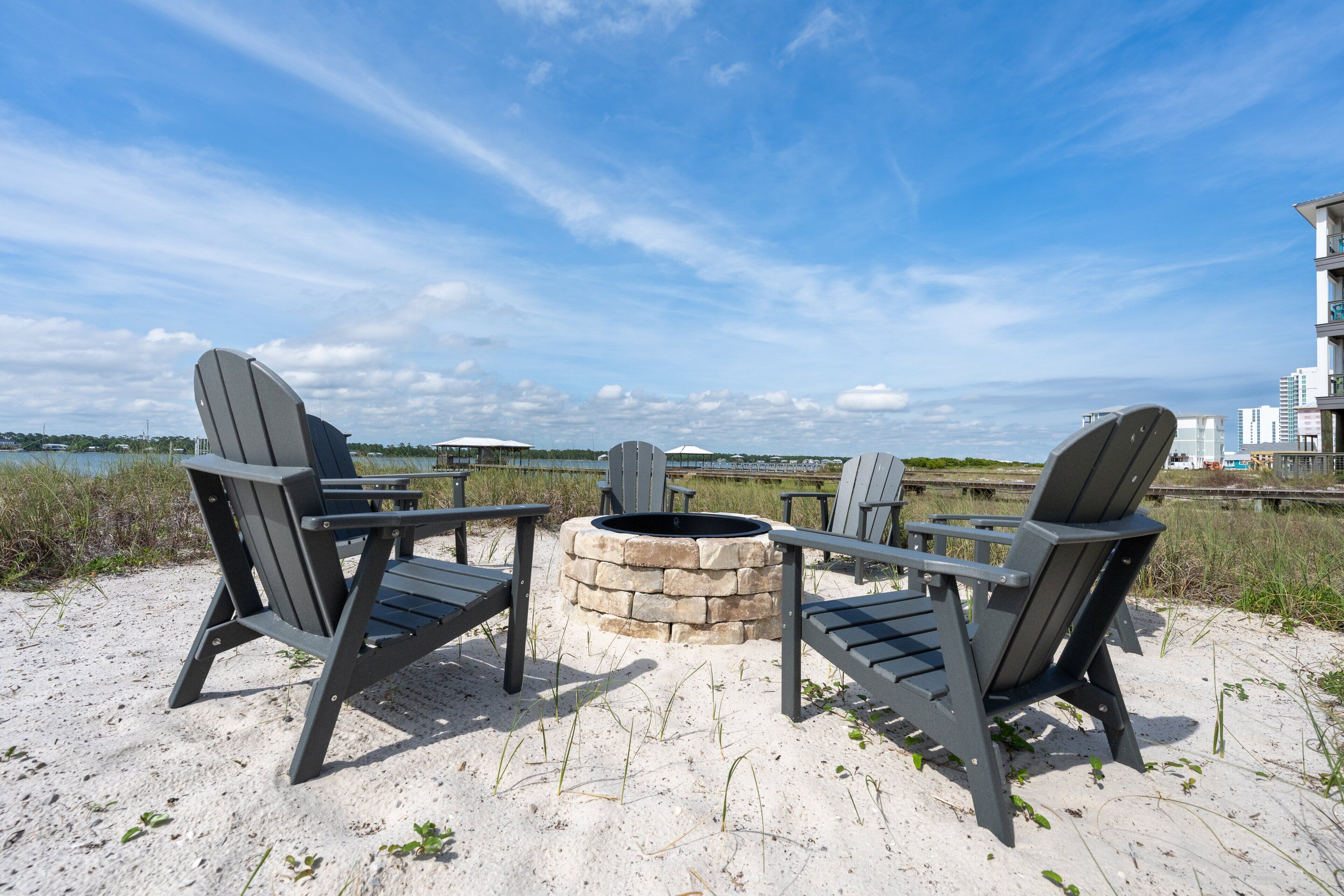A beachside seating area with Adirondack chairs and a stone fire pit.