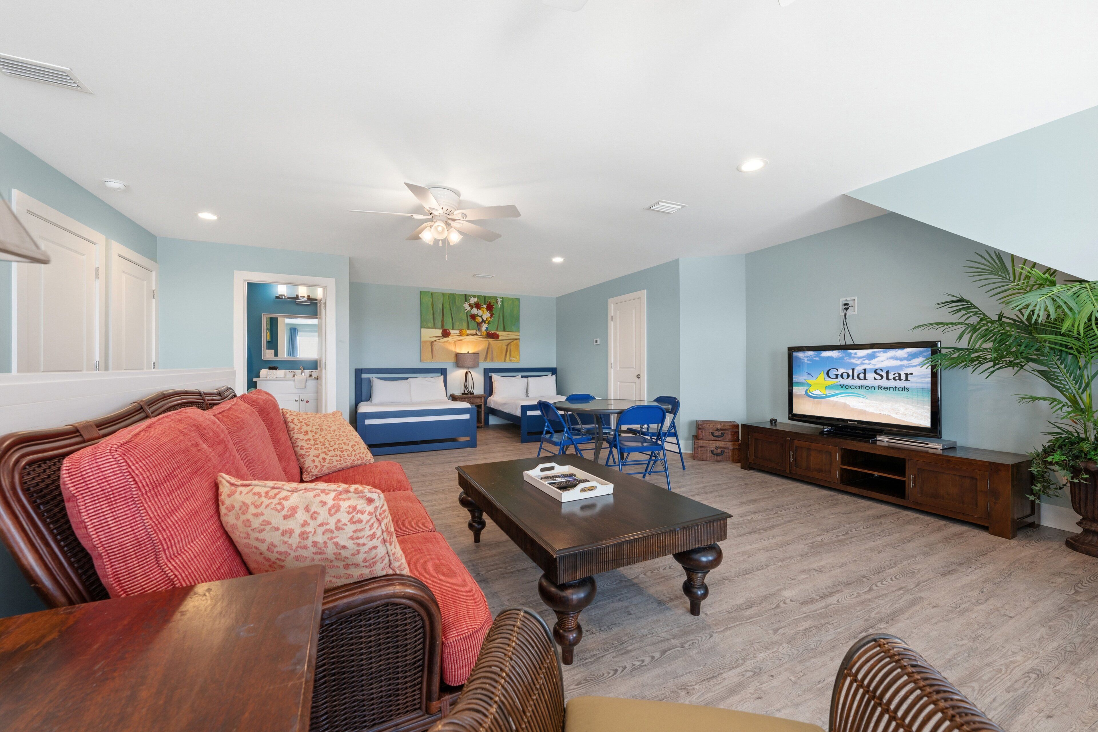 A living room with a television, wicker furniture, a dining area, and a ceiling fan.