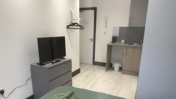 Une pièce avec un lit, un téléviseur posé sur un meuble, un petit bureau et une salle de bain visible au fond.