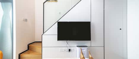 A modern living room with a flat-screen TV mounted on a wall, a wooden staircase, a white sofa, and a small table with a remote control.