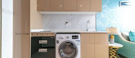 A compact kitchen with a built-in washer, oven, and sink; a green sofa with a gold table; and a marble backsplash.