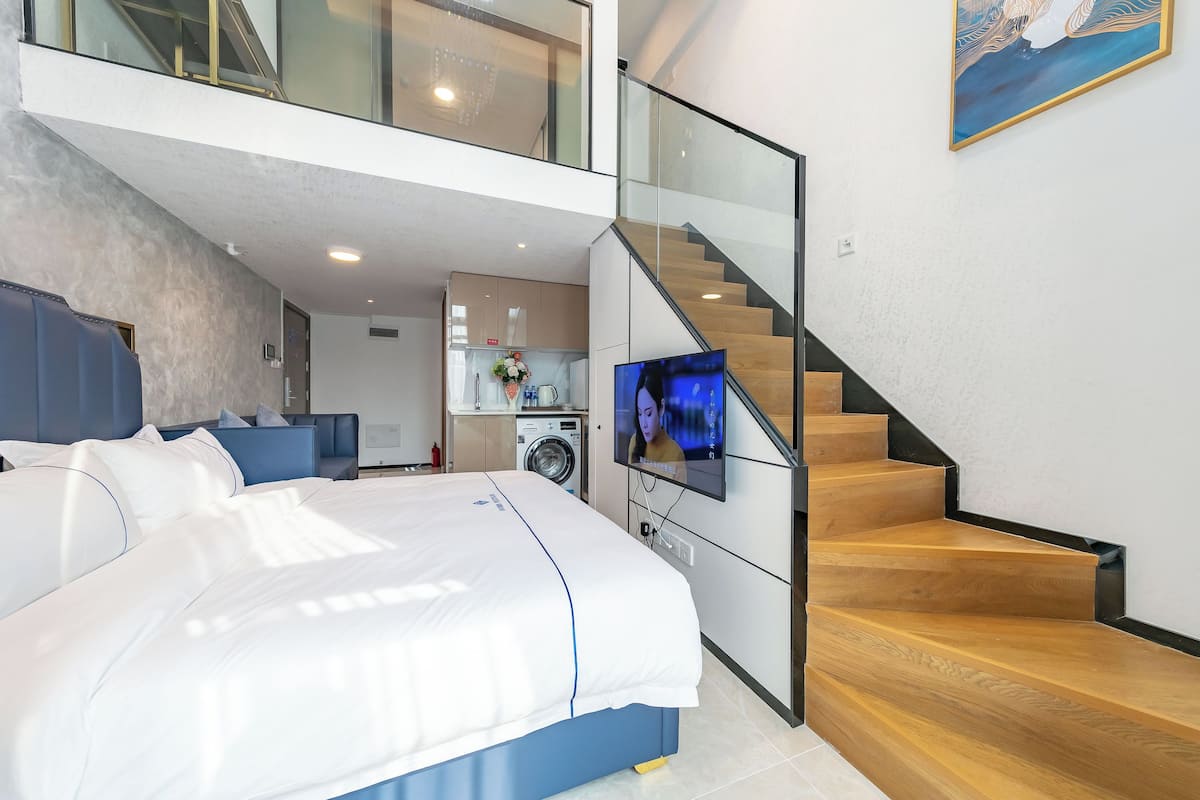 A modern bedroom with a large bed, a TV, and a staircase leading to an upper level.