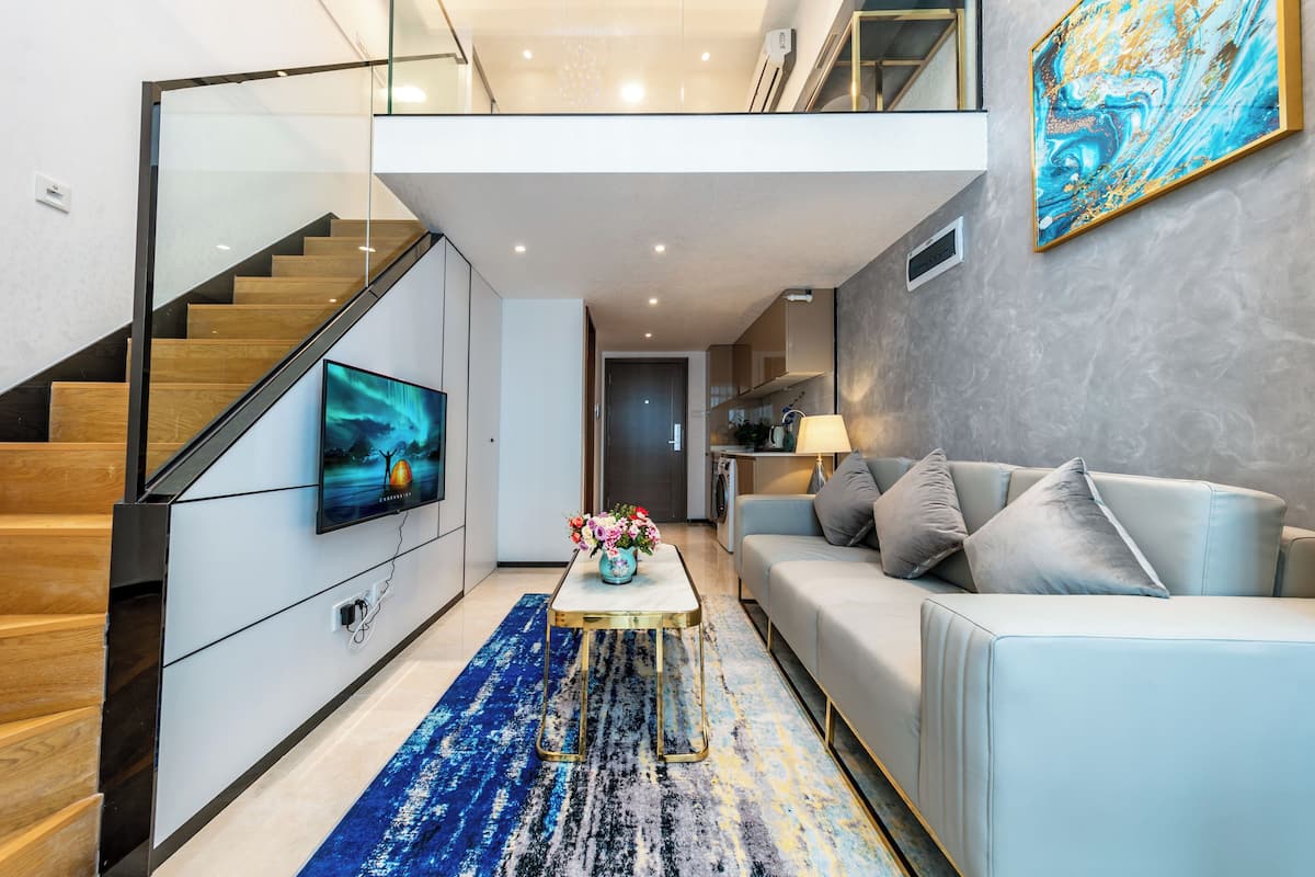 A modern living room with a staircase, a flat-screen TV, a sofa, and a coffee table.