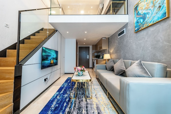 A modern living room with a staircase, a flat-screen TV, a sofa, and a coffee table. - Huaqiang North Executive Apartment (Shenzhen)