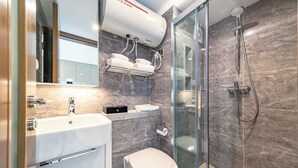Un baño moderno con cabina de ducha de vidrio, inodoro blanco, lavamanos integrado y un perchero para toallas.