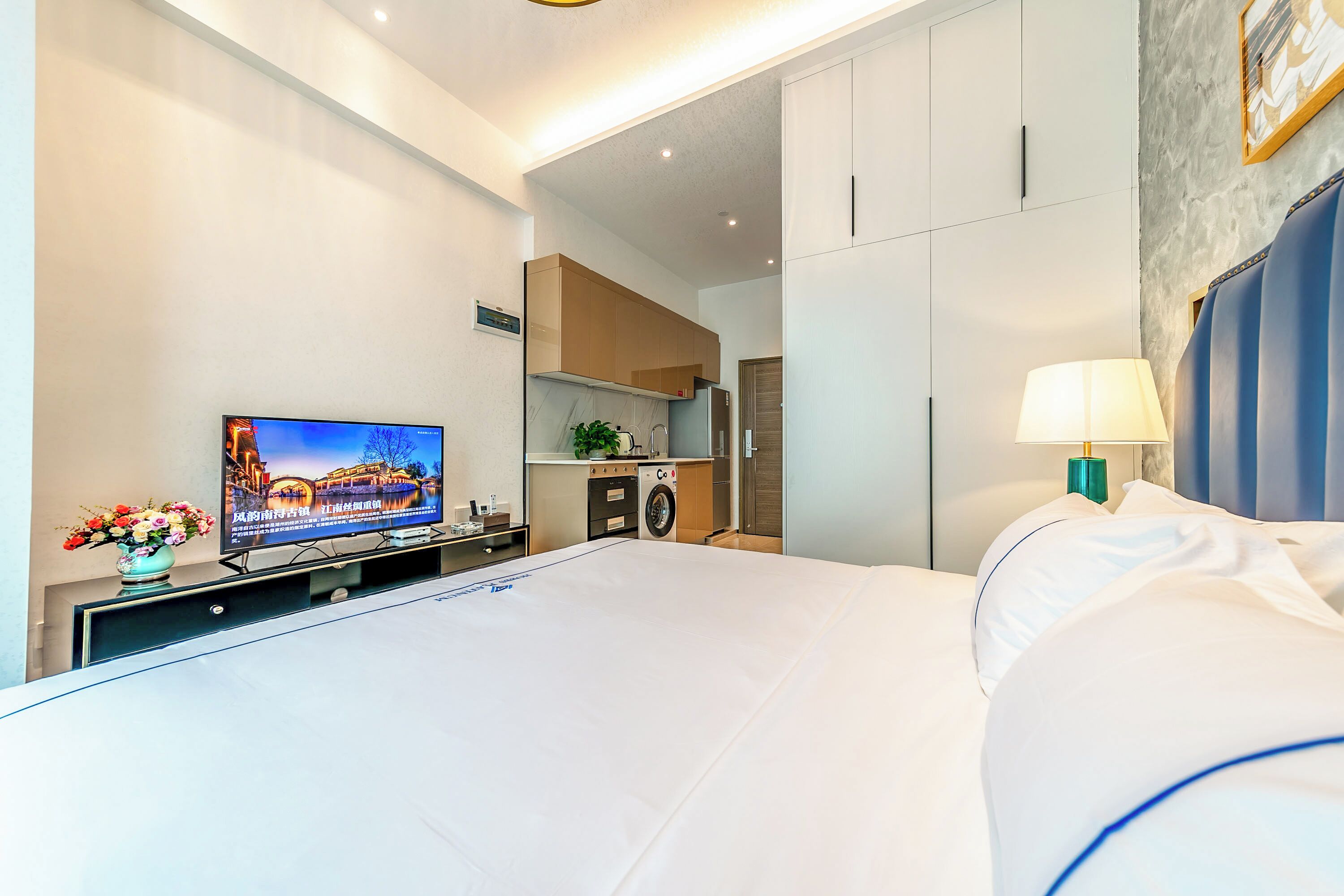 A hotel room with a bed, a television, a washing machine, and a dining area.