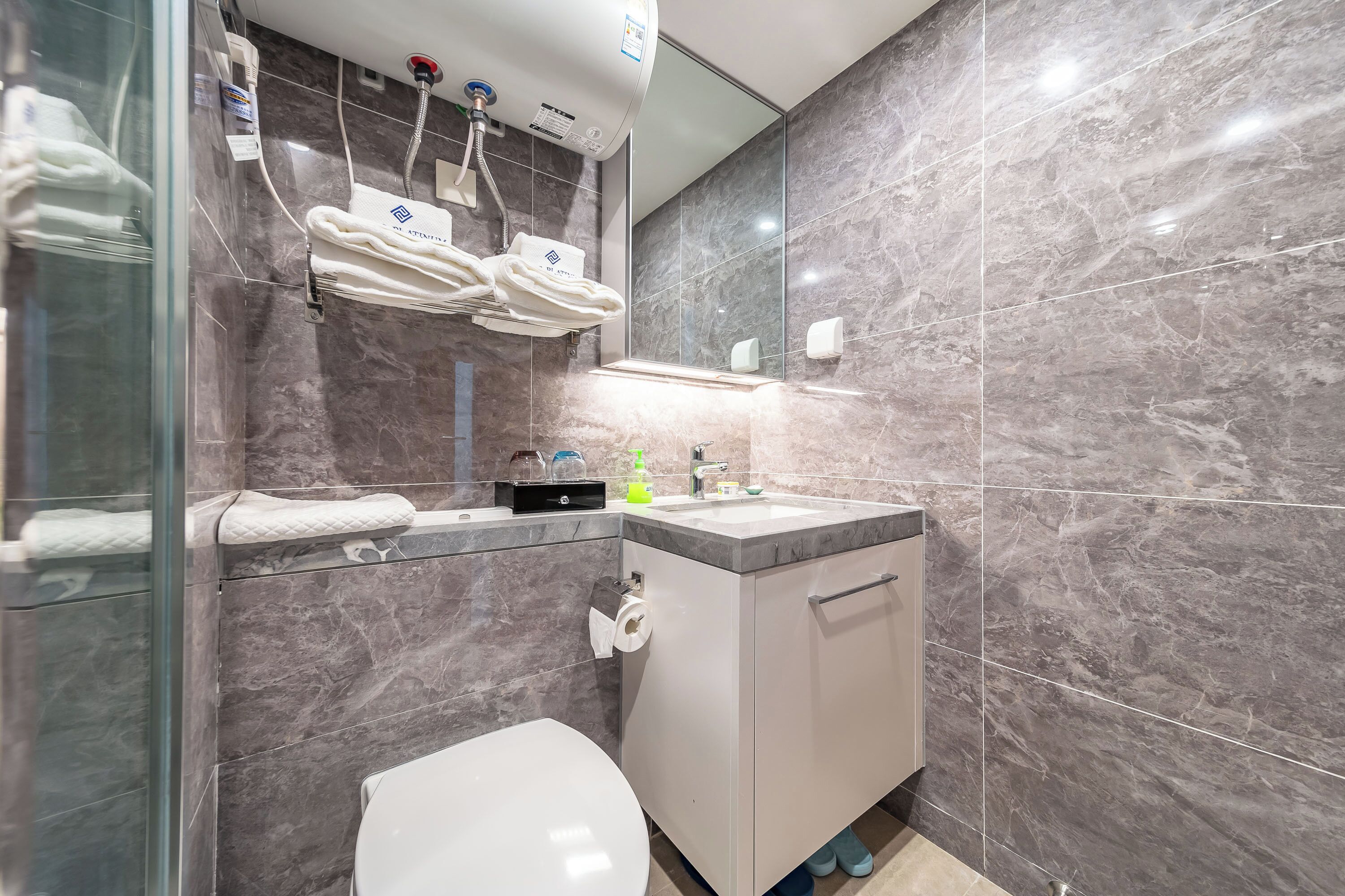 Un baño moderno con cabina de ducha de vidrio, inodoro blanco, pared con azulejos de mármol y lavabo con espejo sobre él.