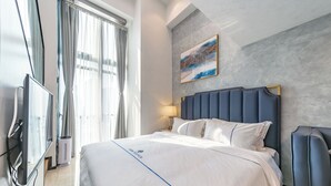 Una habitación de hotel con cama, televisión, ventana con cortinas, un cuadro en la pared y una lámpara.