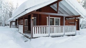 Uma cabana de madeira com varanda, rodeada por árvores cobertas de neve.