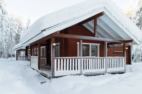 A wooden cabin with a porch, surrounded by snow-covered trees.