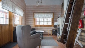 Interior acolhedor de uma cabana com um sofá, uma mesinha, uma janela com vista e uma escada de madeira.