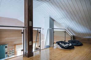 A high-ceilinged room with a wooden floor, a large window, and a metal railing.