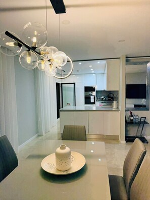 Un comedor moderno con una mesa, sillas, un aplique decorativo y una cocina al fondo.