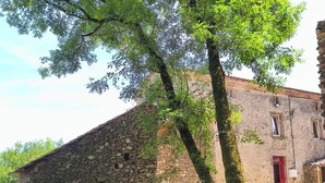 Un bâtiment rustique en pierre, avec une porte rouge, un vélo et un arbre devant.