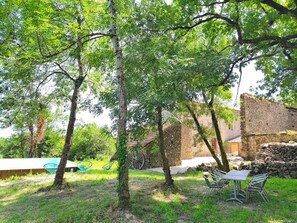 Área externa com árvores, muro de pedra e assentos ao ar livre.