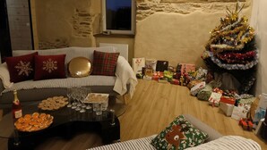 Un salon chaleureux avec un mur en pierre, une fenêtre, un sapin de Noël et un canapé agrémenté de coussins à rayures.