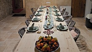 Une longue table à manger, dressée avec des assiettes, des verres et un panier de fruits.