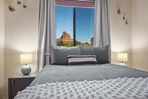 A bedroom with a bed, two bedside tables, a window with curtains, and a view of a mountain. - Iconic Red Rock Views, Luxury Southwest Style with (Sedona)