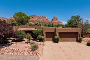 A house with a garage, surrounded by a landscaped garden with various shrubs and a clear view of red rock formations in the background. - Iconic Red Rock Views, Luxury Southwest Style with (Sedona)