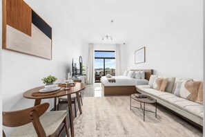 A modern hotel room with a dining area, a sofa, a coffee table, and a view of the city. - Free housekeeping visits during your stay - StayShort - Relaxing Studio in Arjan that Sleeps 3 (Arjan)