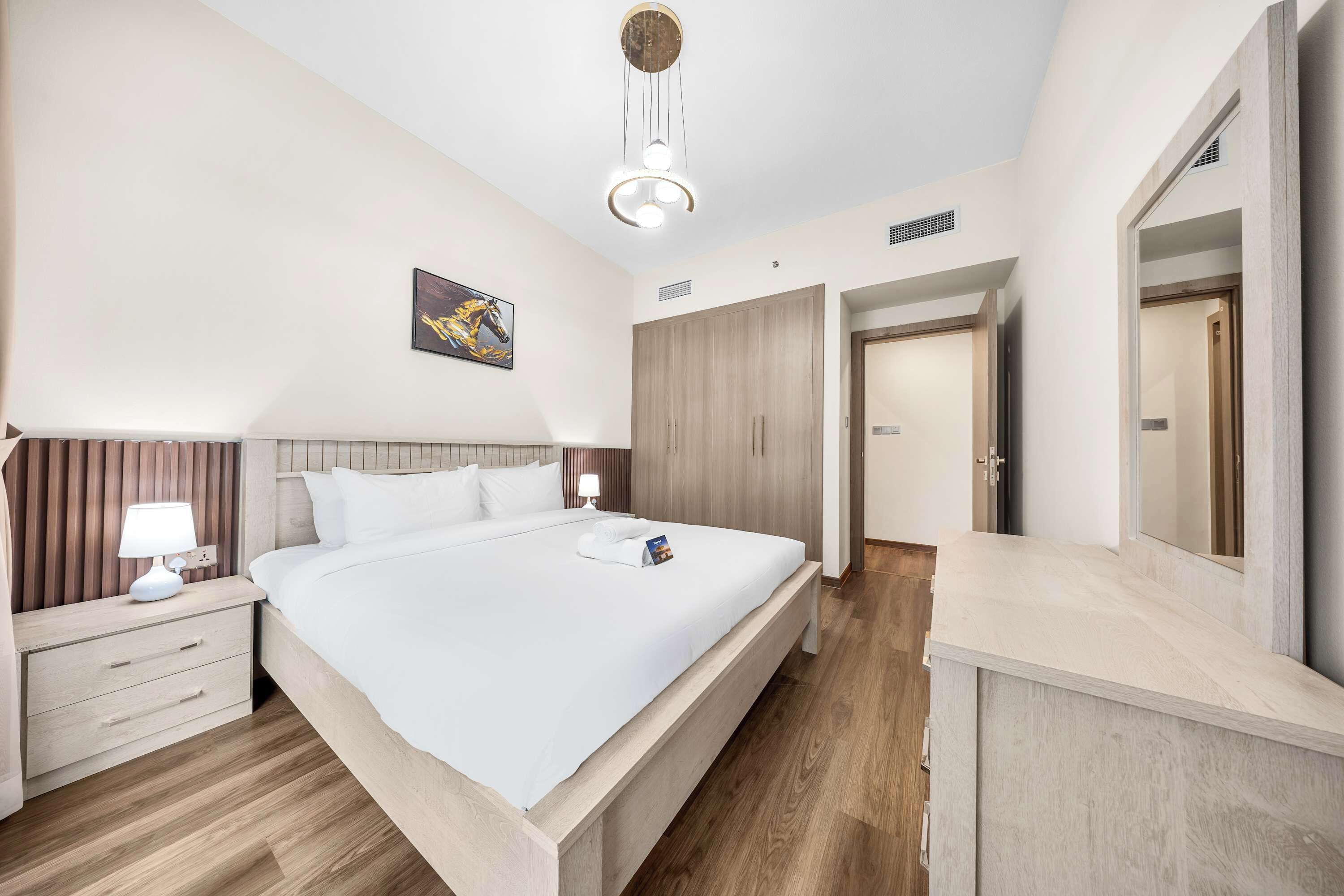 A hotel room with a bed, bedside tables, a mirror, a wardrobe, and a ceiling light fixture.