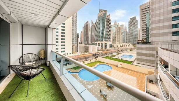 A balcony with a view of a cityscape, a pool, and a lounge area. - StayShort - Chic 1BR Sleeps 2 in Dubai Marina Near Metro (Dubai Marina)