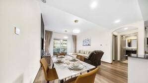 A modern dining area with a long table, chairs, and a kitchen in the background. - StayShort - Chic 1BR Sleeps 2 in Dubai Marina Near Metro (Dubai Marina)