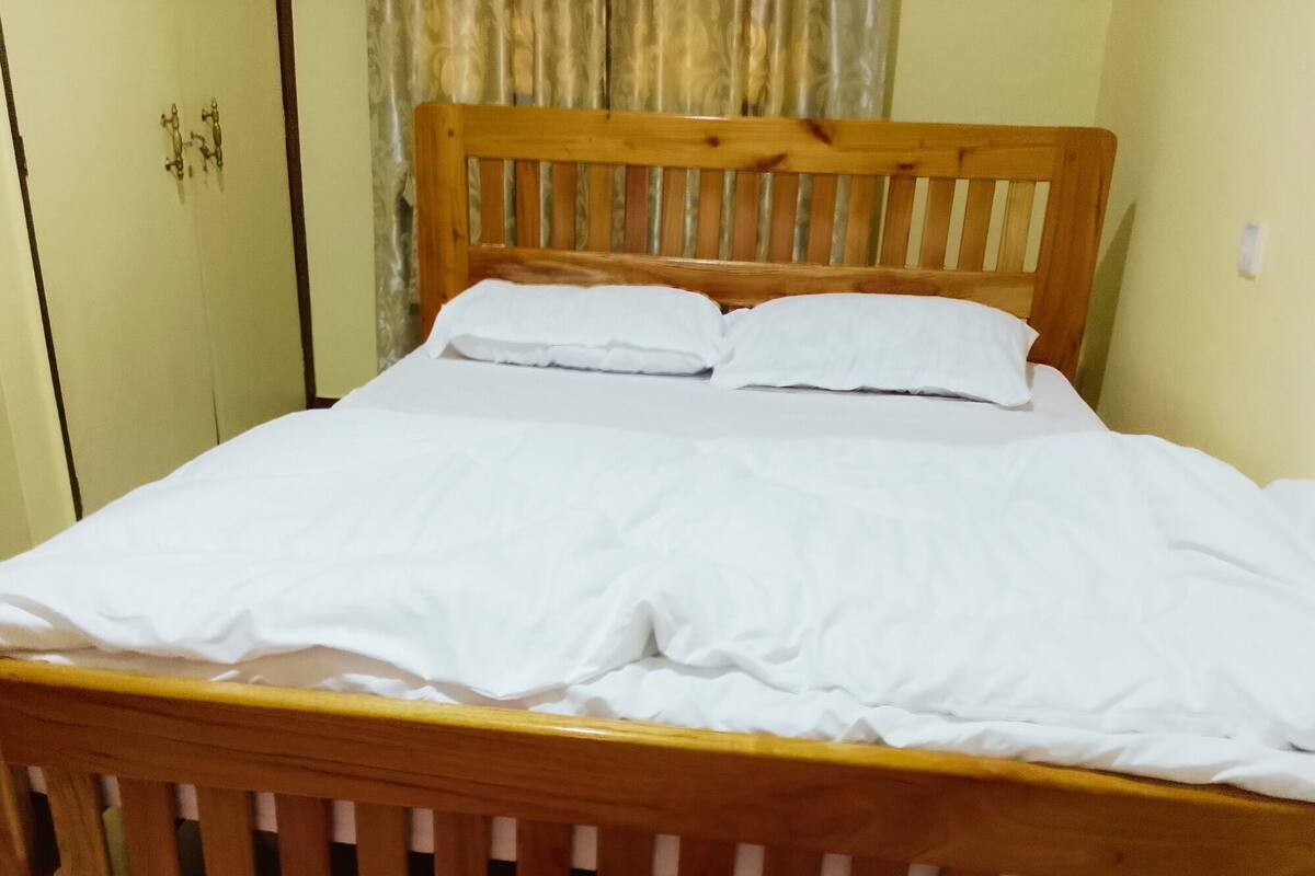 Uma cama de madeira com roupa de cama branca num quarto com parede verde e cortina.