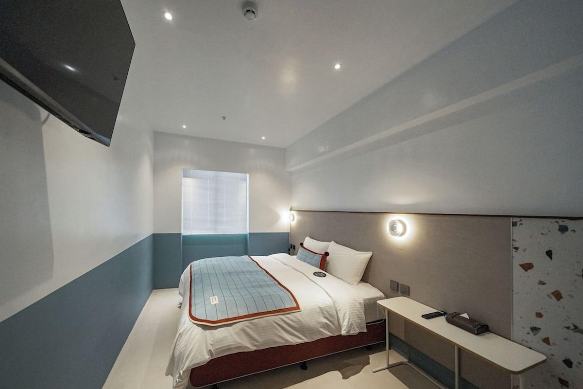 A modern hotel room with a bed, bedside table, and a window.