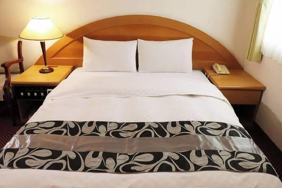 Una habitación de hotel con cama, lámpara de noche, teléfono y mesita de noche.