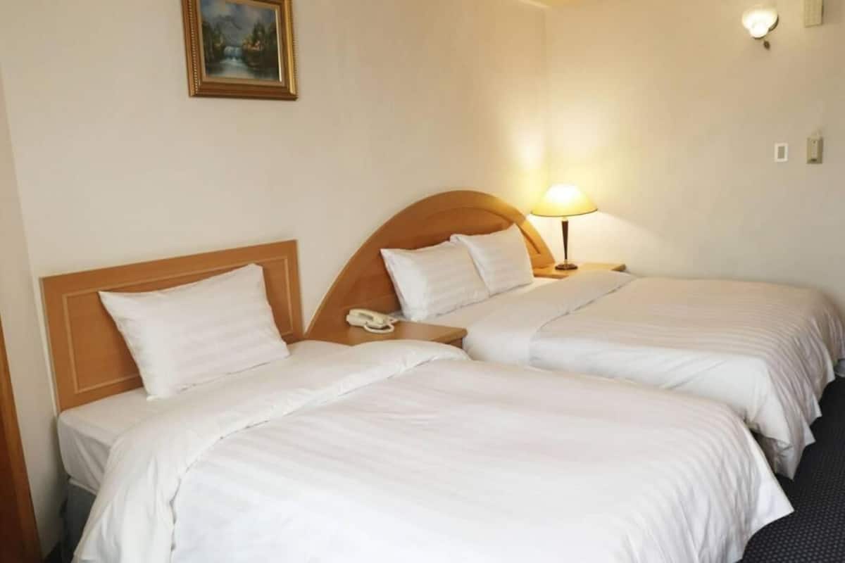 Habitación de hotel con dos camas, una lámpara de noche, un teléfono en la mesita de noche y un cuadro en la pared.