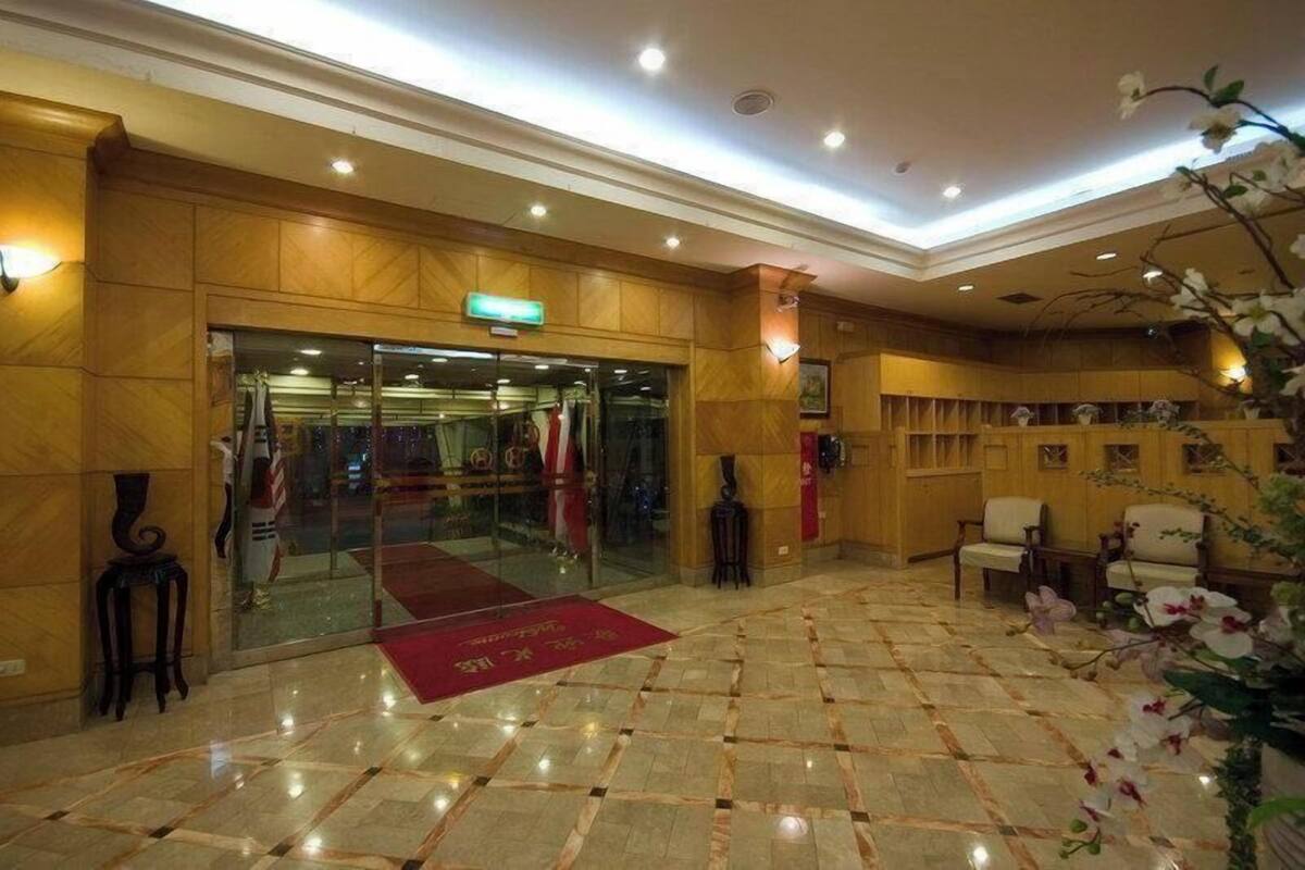 Vestíbulo de hotel con piso de mármol, paneles de madera, un mostrador de recepción y una alfombra roja que conduce a la entrada.