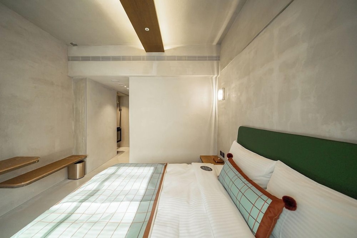 A hotel room with a bed, bedside tables, and a green headboard.