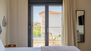 Un dormitorio con cama, puerta corrediza al balcón, una mesita pequeña y una silla.