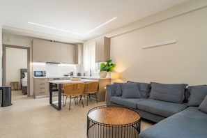 Una sala de estar moderna con un sofá gris, una mesa de centro de madera y una zona de cocina con una mesa de comedor y sillas.