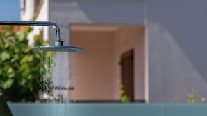 Un cabezal de ducha con agua corriendo, una pared azul y un edificio con un balcón al fondo.