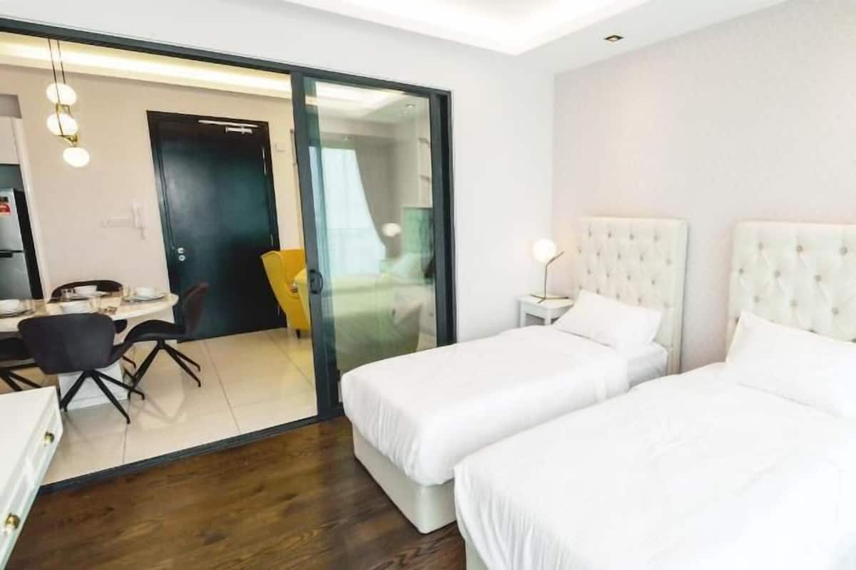 Quarto de hotel com duas camas, uma área de refeições e uma porta de vidro deslizante que dá para uma varanda.
