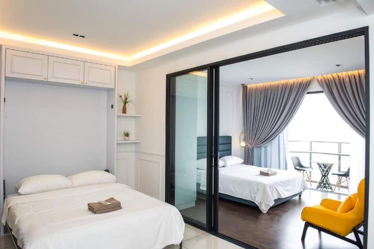 Quarto de hotel moderno com uma cama grande, porta de correr de vidro para uma varanda e decoração luminosa.
